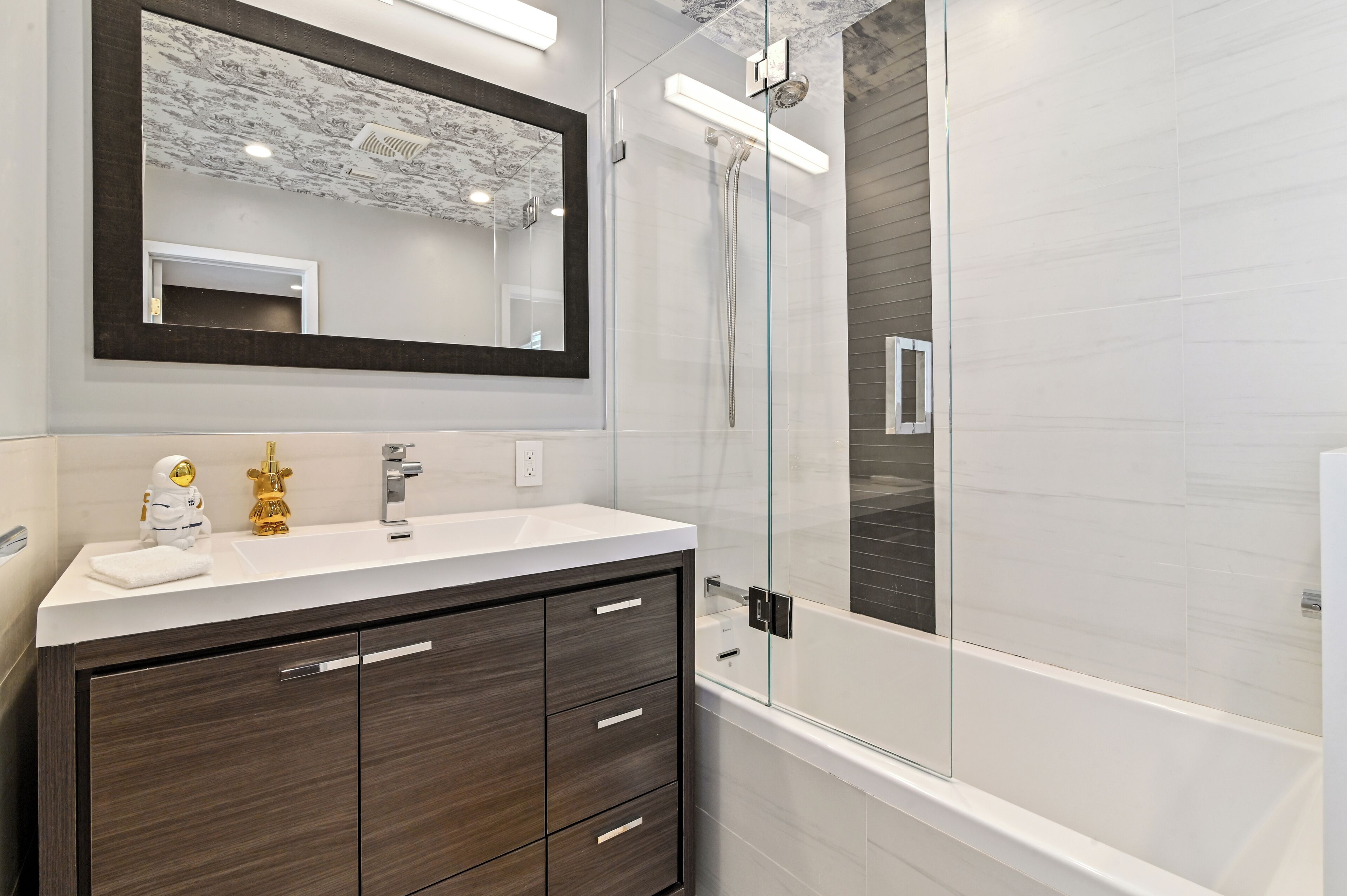 Un baño moderno con tocador de mármol, un espejo grande y una ducha con paredes de cristal.