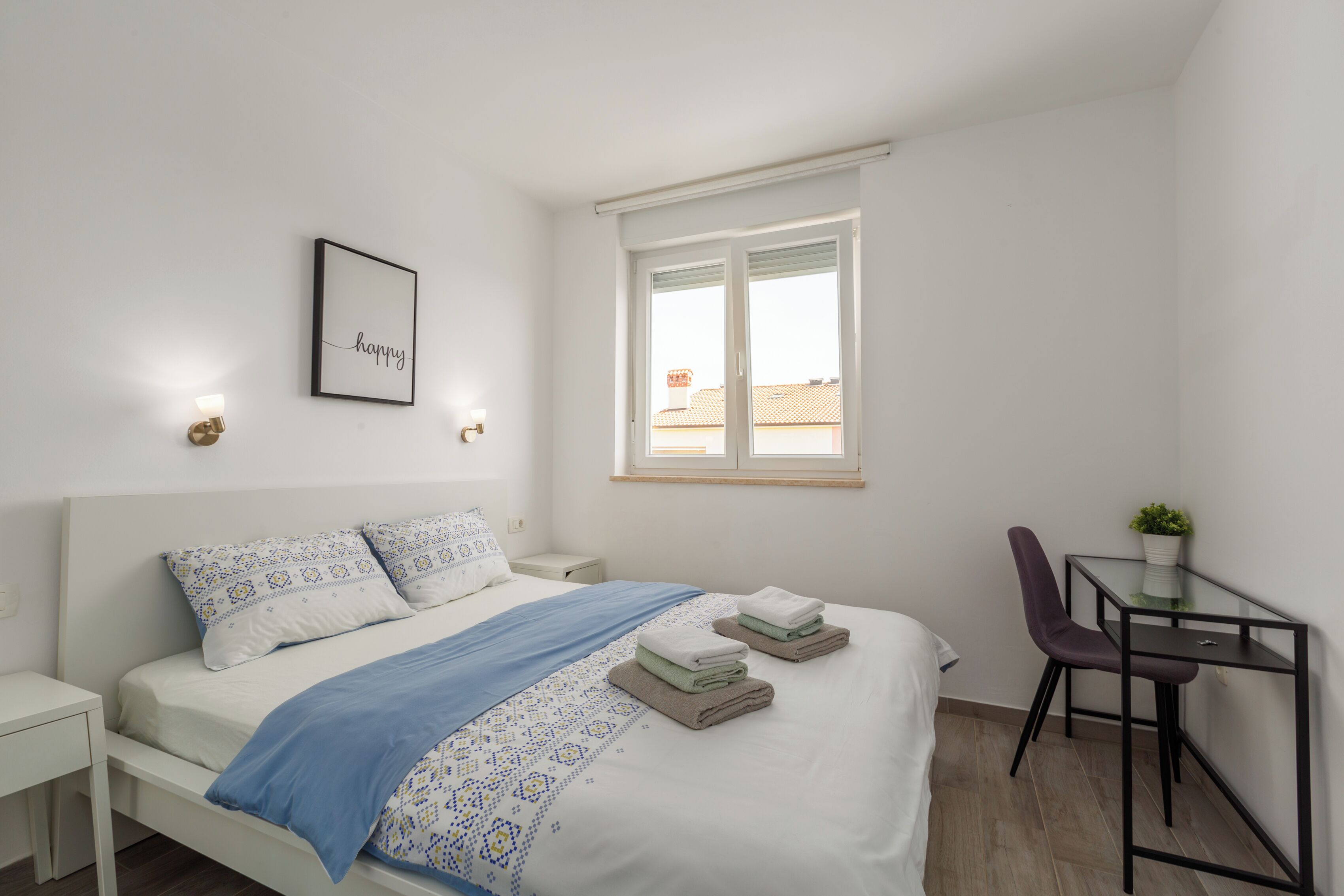 Une chambre moderne et bien éclairée, avec un lit soigneusement fait, un petit bureau et une chaise.