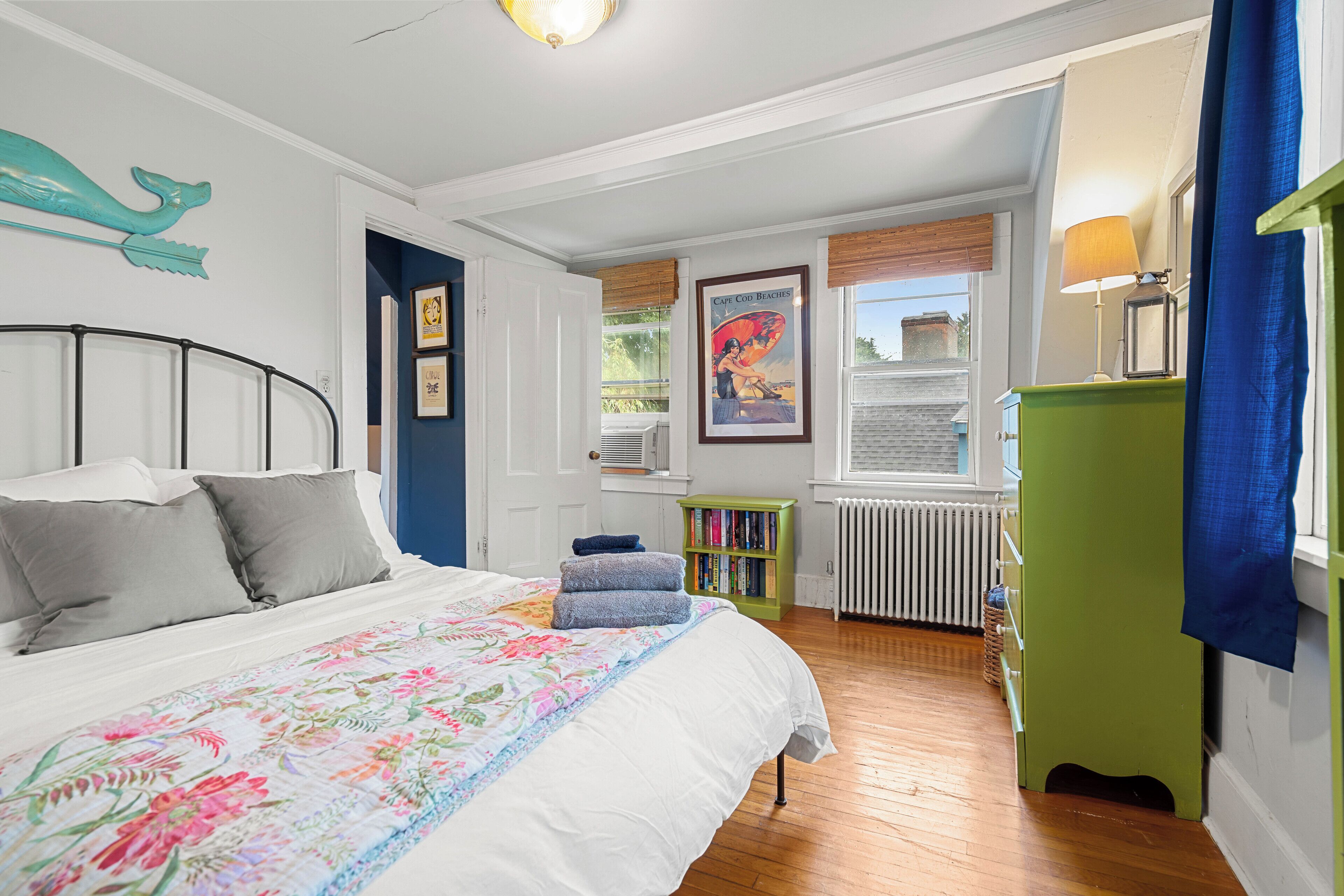 Un dormitorio con cama, estantería, radiador y ventana con vistas al exterior.