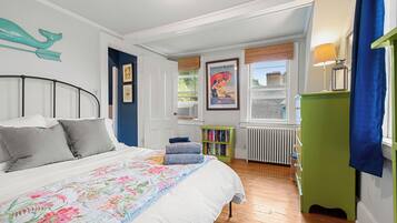 Un dormitorio con cama, estantería, radiador y ventana con vistas al exterior.