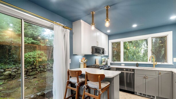 A modern kitchen with a large island, white cabinets, and a view of a garden through a sliding glass door. - 2BR Historic Marblehead Home+Minutes to Beach (Marblehead)