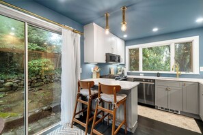 Een moderne keuken met een groot eiland, witte kasten en uitzicht op een tuin door een schuifdeur van glas.