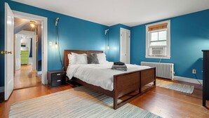 A bedroom with a wooden bed, a nightstand, a radiator, and a window with blinds. - 2BR Historic Marblehead Home+Minutes to Beach (Marblehead)