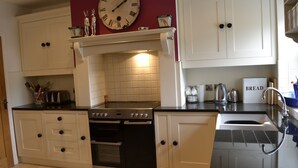 A kitchen with white cabinets, a black stove, a sink, and a clock on the wall. - 4 bedroom accommodation in Hawes (Hawes)