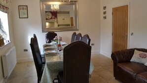 A dining area with a table set for four, a chandelier, a large mirror, and a brown leather sofa. - 4 bedroom accommodation in Hawes (Hawes)
