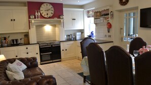 A kitchen with white cabinets, a clock, and a dining area with a table and chairs. - 4 bedroom accommodation in Hawes (Hawes)