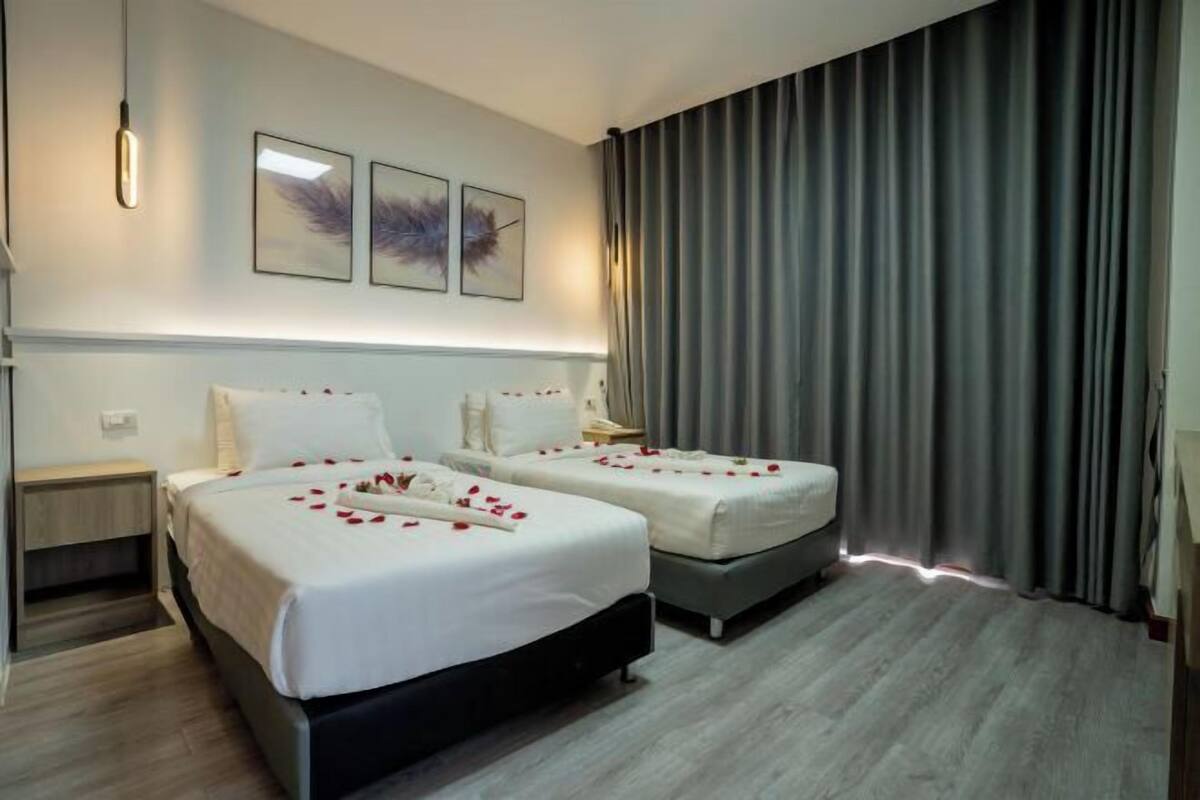 A hotel room with two beds, a nightstand, a lamp, and a large window with curtains.