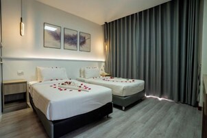 Habitación de hotel con dos camas, una mesita de noche, una lámpara y un amplio ventanal con cortinas.