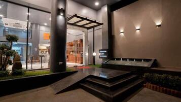 A modern hotel lobby with a reception desk, a seating area, and a display board.