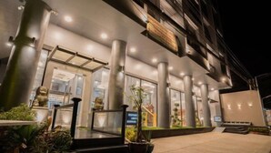 Una entrada de hotel moderna con fachada de vidrio, columnas grandes e iluminación exterior.