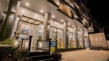 A hotel entrance with a modern design, featuring a glass facade, columns, and outdoor lighting.