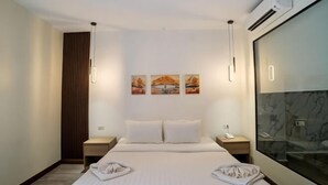 Habitación de hotel con cama, mesitas de noche, equipo de aire acondicionado y una obra de arte en la pared.