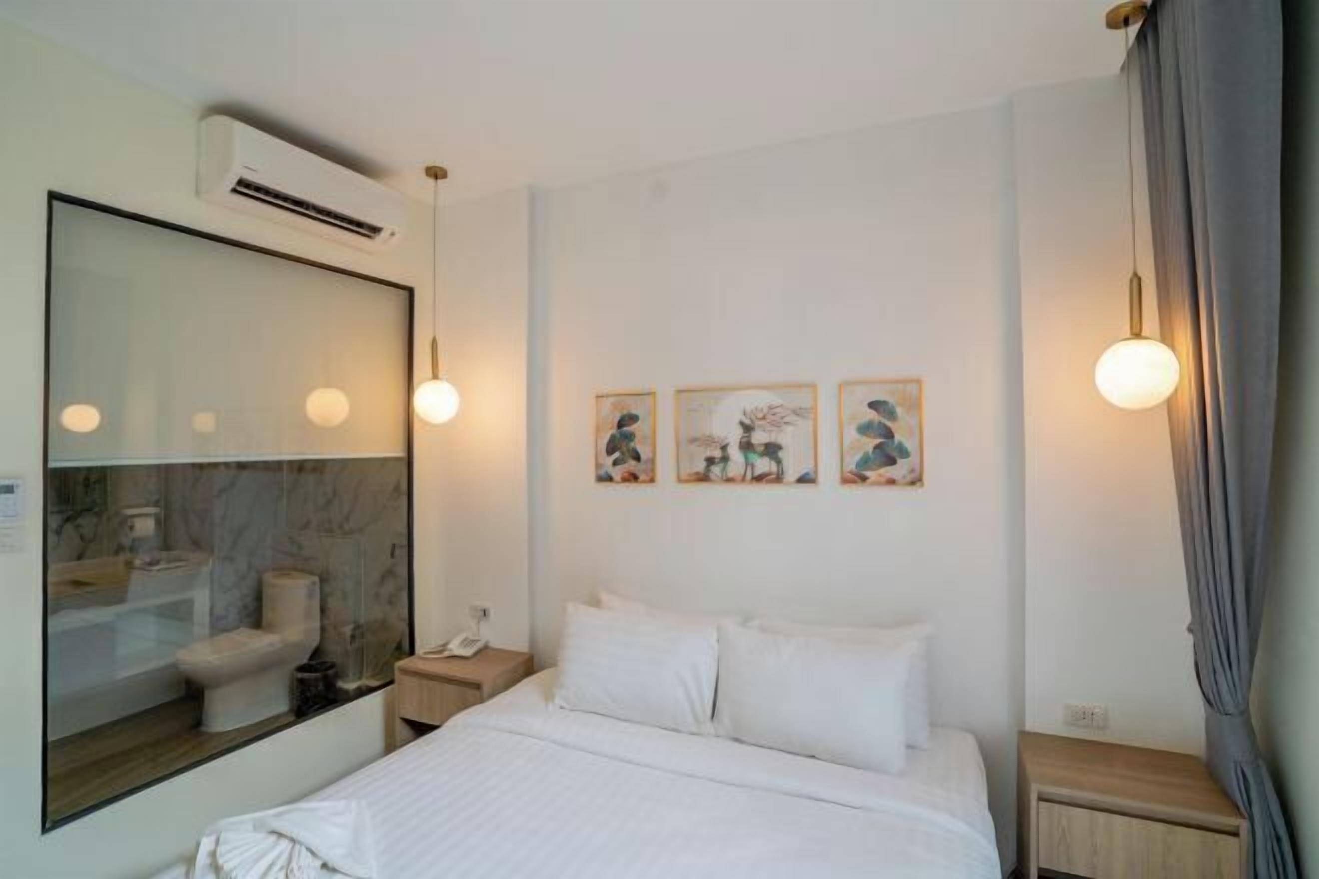 A hotel room with a bed, bedside table, lamp, and artwork on the wall.