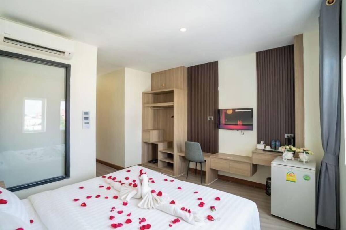 A hotel room with a bed, a desk, a chair, a wardrobe, a mirror, and a small fridge.