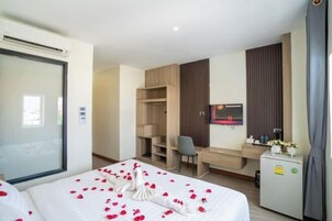 Habitación de hotel con cama, escritorio, silla, armario, espejo y un refrigerador pequeño.