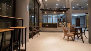Un interior de cafetería moderna con piso de mármol, mesas y sillas de madera, y un letrero que dice 'COFFEE MILL'.