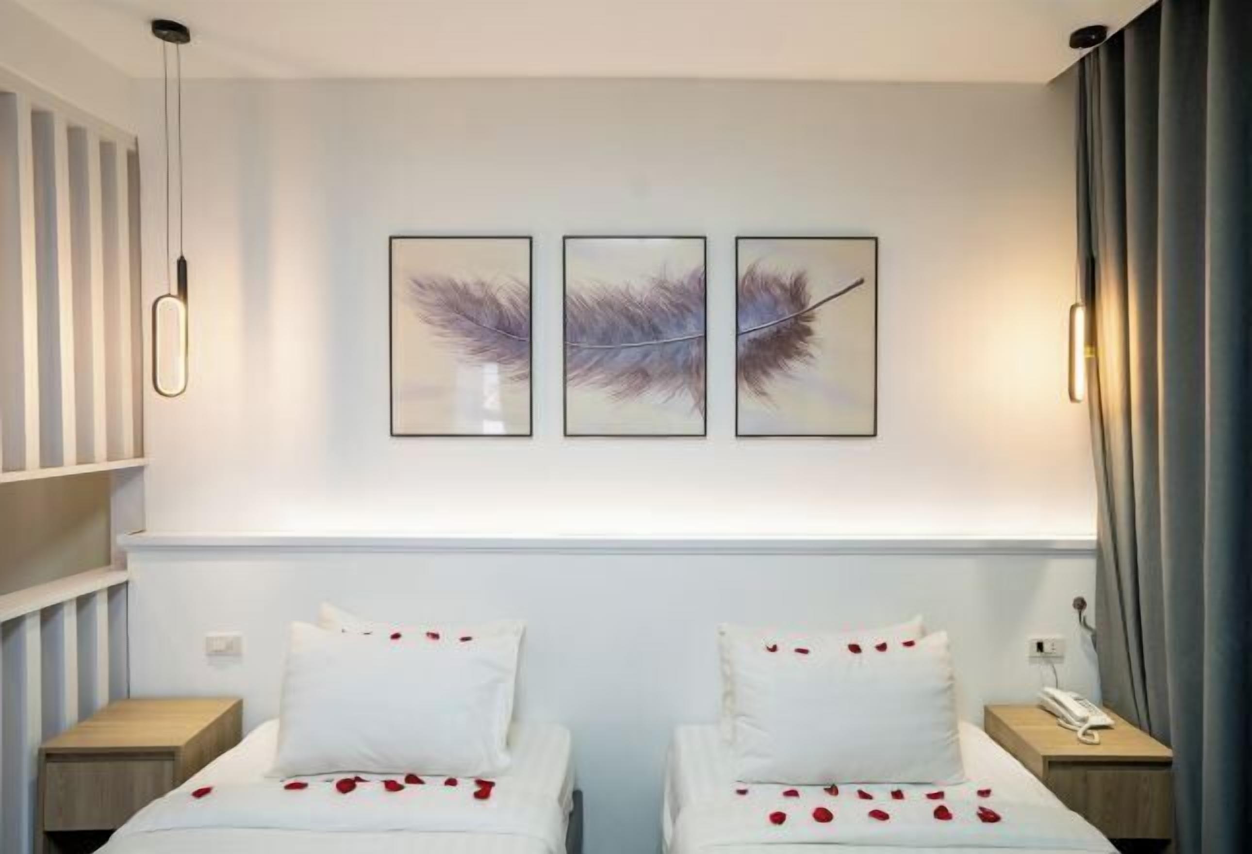 A hotel room with two beds, a bedside table with a phone, and a wall-mounted artwork of feathers.