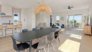 A modern kitchen with white cabinets, a dining area with a dark table and chairs, and a living area with a sofa and coffee table.