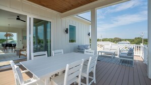 A covered outdoor deck with a white table and chairs, a glass door leading inside, and a view of the surrounding landscape.