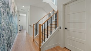 A hallway with a wooden staircase, a white door, and a wall with a tropical mural.