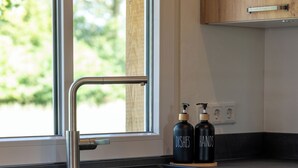 A modern kitchen with a stainless steel faucet, wooden cabinets, and a window with a view of greenery. - Weitblick- Ruhepol in Münsterländer Parklandschaft (Dülmen)