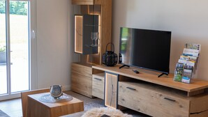 A modern living room with a flat-screen TV, wooden cabinets, a sofa, and a dining area. - Weitblick- Ruhepol in Münsterländer Parklandschaft (Dülmen)