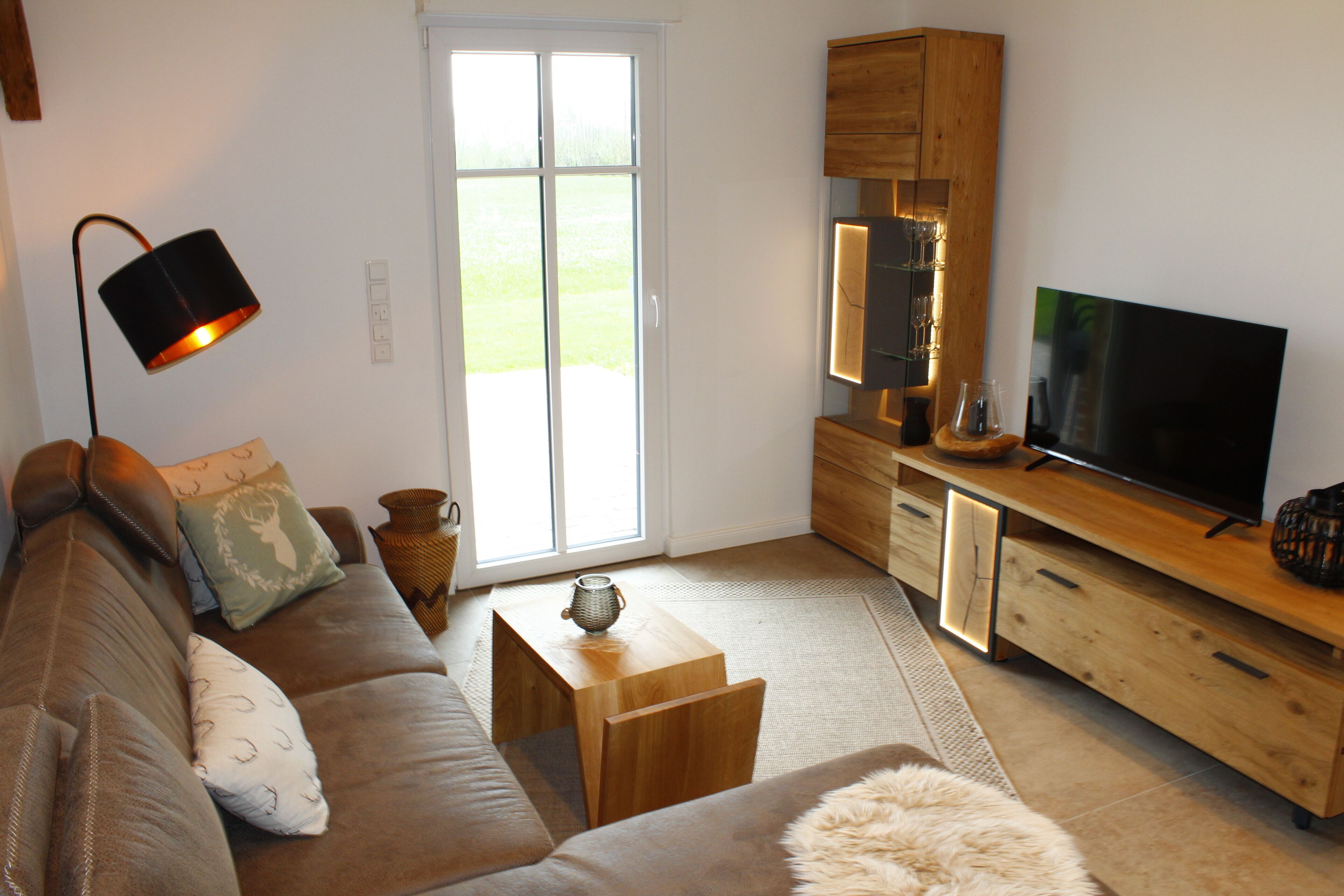 A modern living room with a brown leather sofa, a wooden coffee table, a television on a wooden stand, and a lamp.