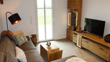 A modern living room with a brown leather sofa, a wooden coffee table, a television on a wooden stand, and a lamp.