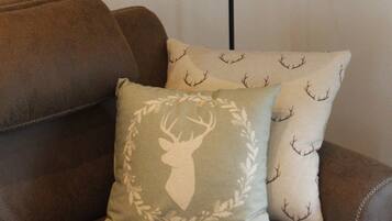 A brown leather sofa with two decorative pillows, one with a deer motif and the other with antlers. A black floor lamp with a gold shade is positioned behind the sofa.