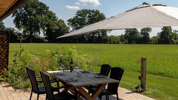 An outdoor patio with a table and chairs, a large umbrella, and a view of a grassy field. - Weitblick- Ruhepol in Münsterländer Parklandschaft (Dülmen)