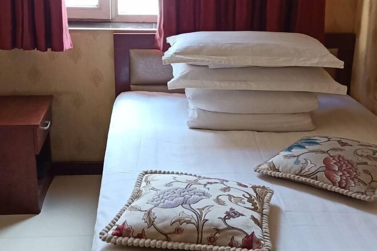 A neatly made bed with white linens and decorative pillows, a wooden nightstand, and a window with curtains.