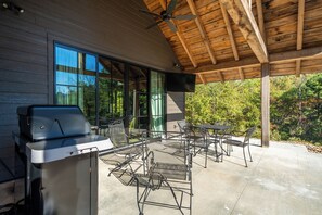 An outdoor patio with a grill, metal chairs, and a ceiling fan.