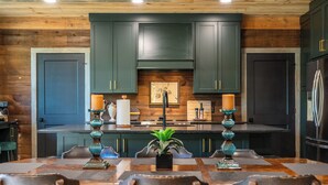 Una cucina moderna con pensili verde scuro, un'isola centrale con una pianta e un frigorifero in acciaio inossidabile.