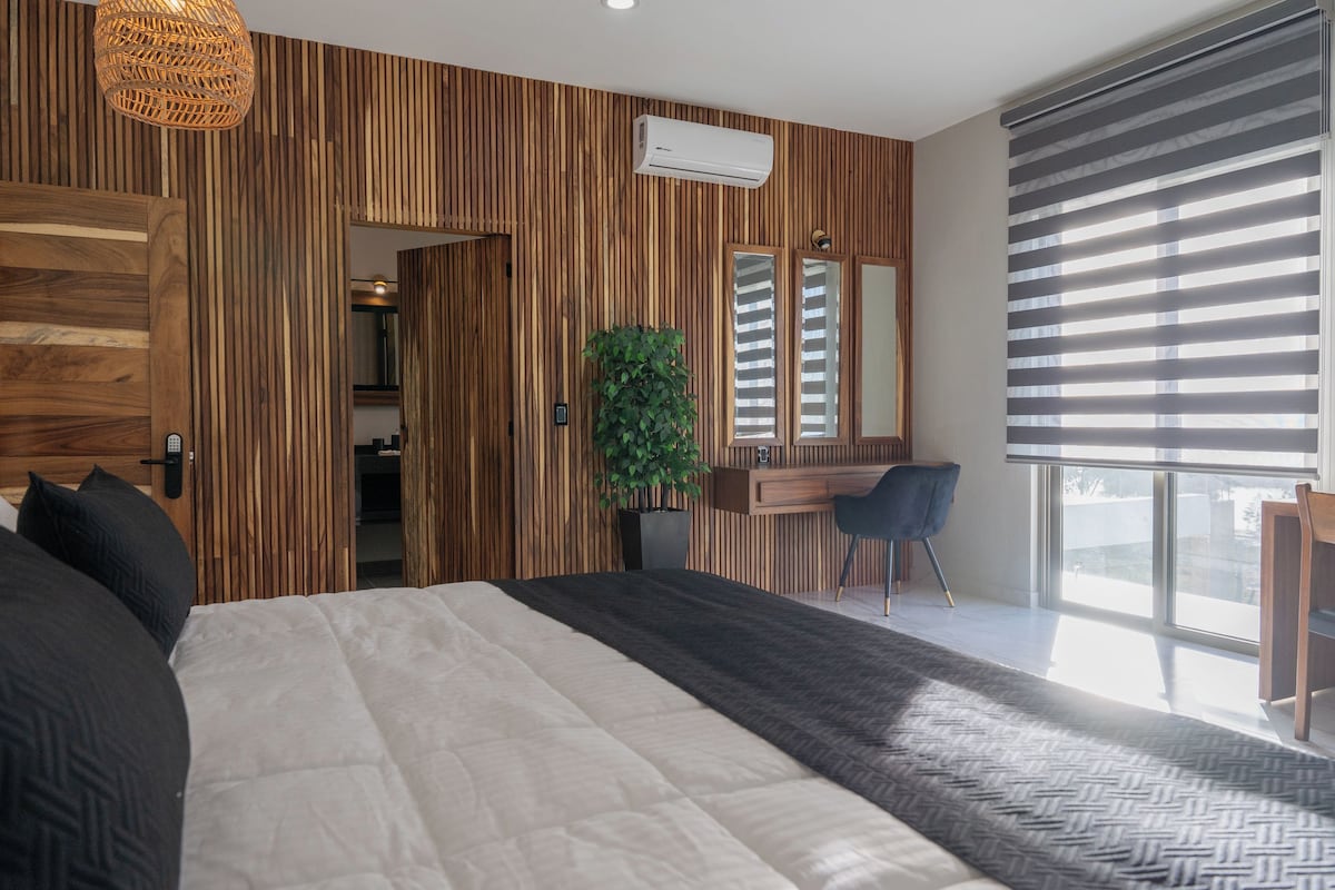Ein modernes Schlafzimmer mit einem großen Bett, einem Schreibtisch, einem Sessel und einer Zimmerpflanze.