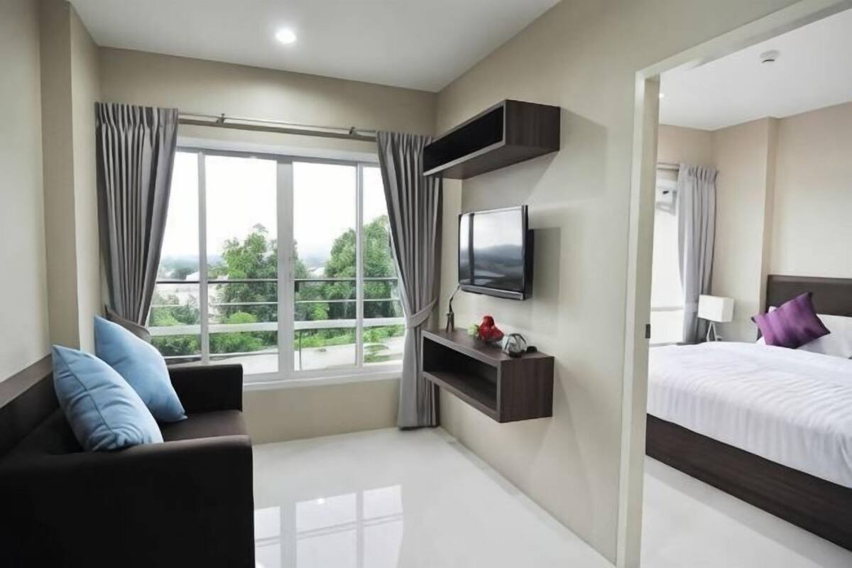 A hotel room with a bed, a TV, a sofa, and a window with curtains.