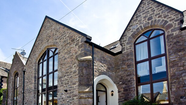 Un edificio de piedra con ventanas de arco y una puerta, con un pequeño jardín delantero.
