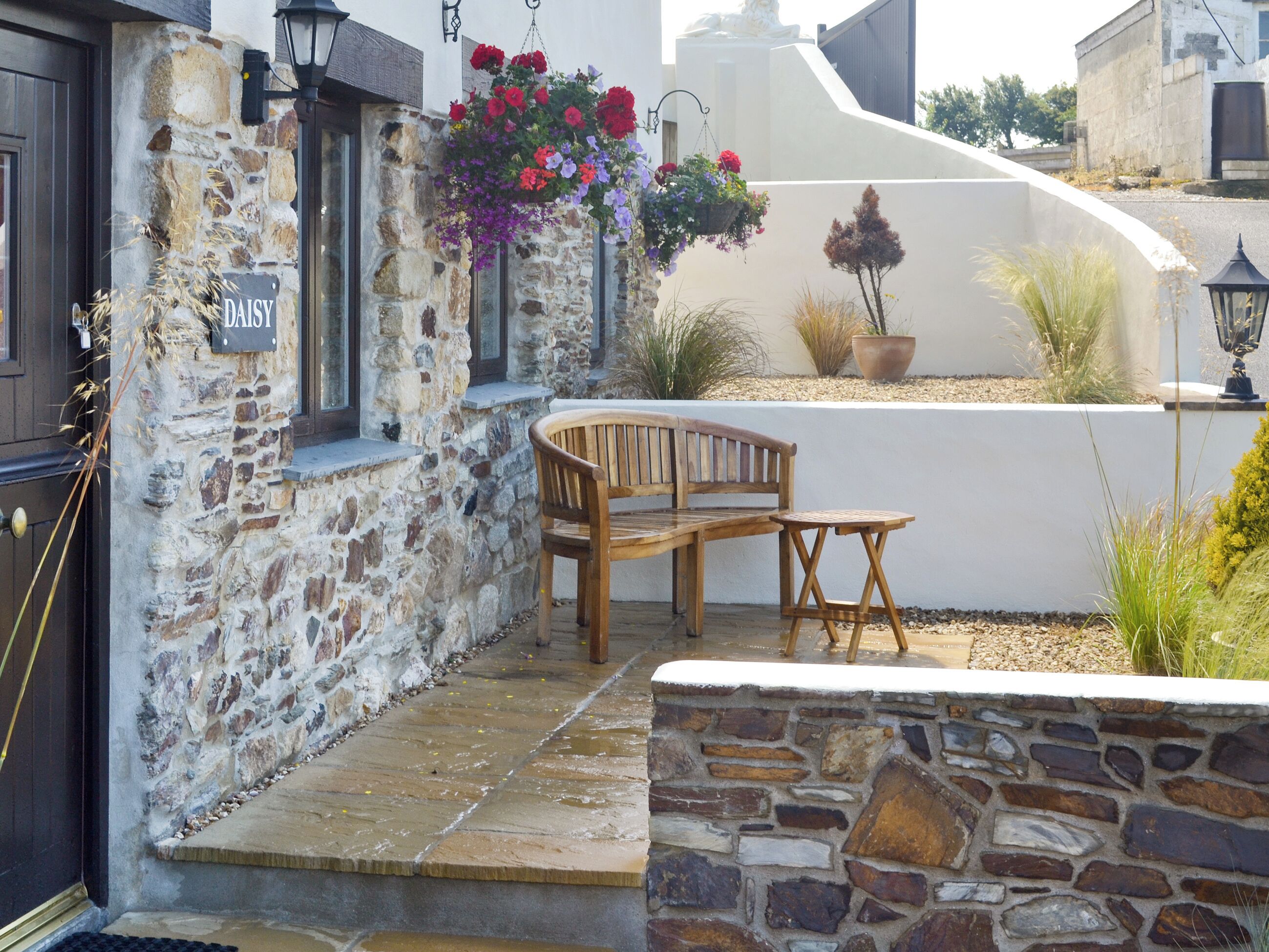 A stone building with a wooden bench and table, a hanging flower basket, and a potted plant.