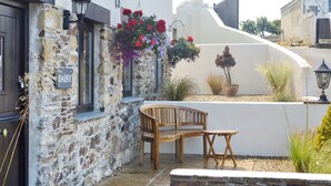Un bâtiment en pierre avec un banc et une table en bois, une jardinière suspendue et une plante en pot.