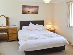 A bedroom with a bed, a nightstand, a dresser, a mirror, and a painting on the wall. - Daisy Cottage - 25931 (Perranporth)