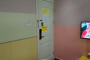 Una habitación con una puerta blanca, un televisor montado en la pared y un armario de madera.