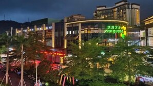 A multi-story building with a prominent 'Vanguard' sign, surrounded by greenery and other commercial establishments. - Zijijia Inn (Shenzhen)