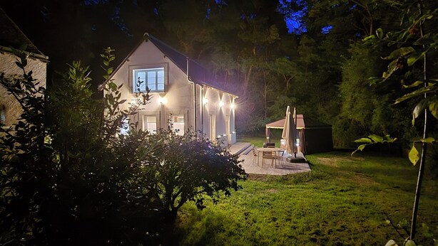 Ein Haus mit einem gut beleuchteten Patio, einer kleinen Terrasse und einem Rasen.