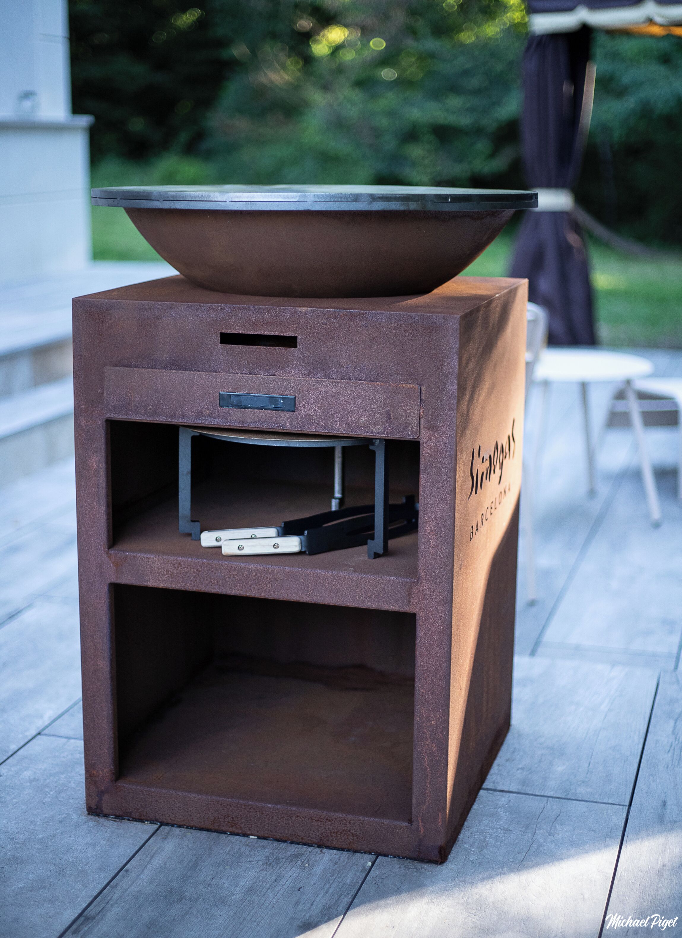 A rustic outdoor grill with a flat top, a shelf with a flat-screen TV, and a side compartment.
