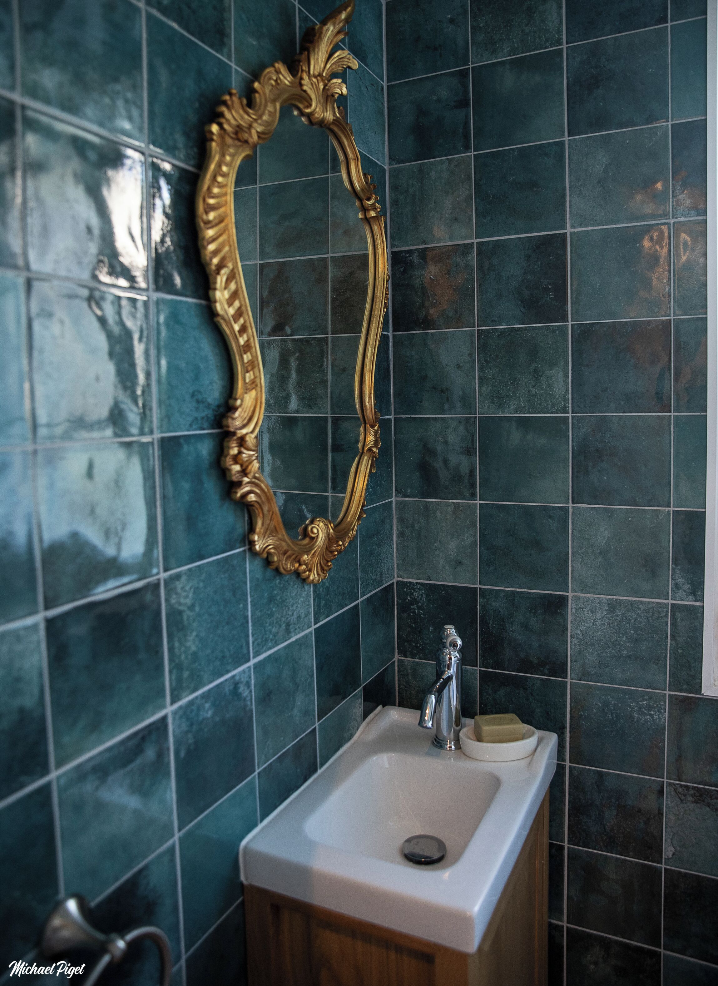 Een badkamer met donkergroene tegels, een witte wastafel en een spiegel met gouden lijst.