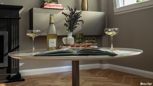 Une table avec une bouteille de vin blanc, deux verres, un livre et un vase contenant des fleurs séchées.