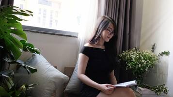 A person sitting on a sofa in a room with a window, a plant, and a vase with flowers.