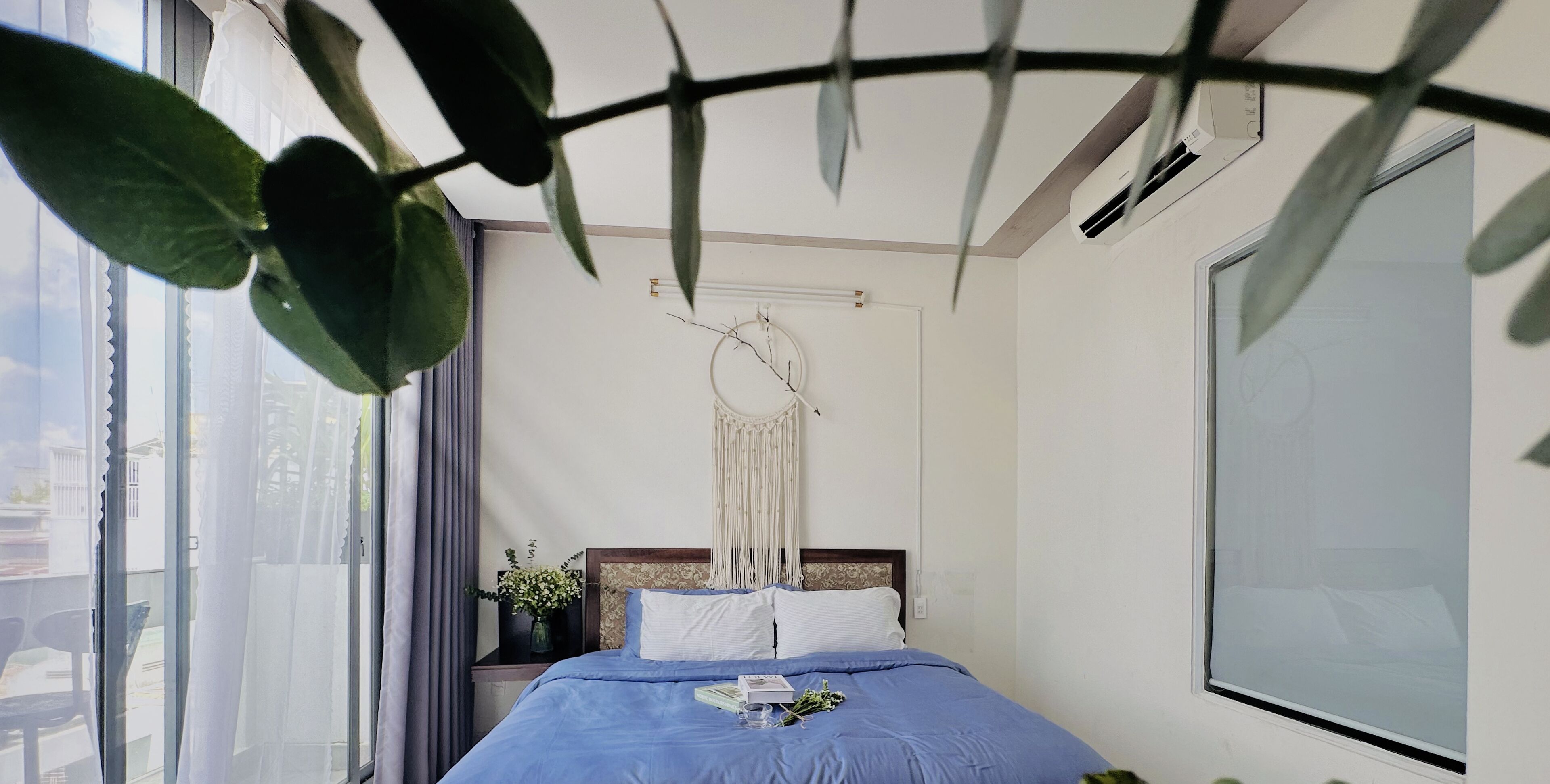A bedroom with a bed, a window, and a macrame wall hanging.