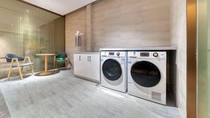 A modern laundry room with two front-loading washing machines, a small table, and two chairs. - Ting HOTEL(Ningbo International Convention Center) (Ningbo)