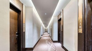 Un long couloir étroit, typique des hôtels, avec des portes des deux côtés, numérotées 301 et 330, et un sol recouvert de moquette.