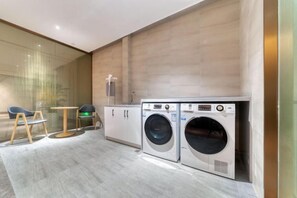 A modern laundry room with two front-loading washing machines, a small table, and chairs. - EGREEN HOTEL(Ningbo International Convention Center) (Ningbo)